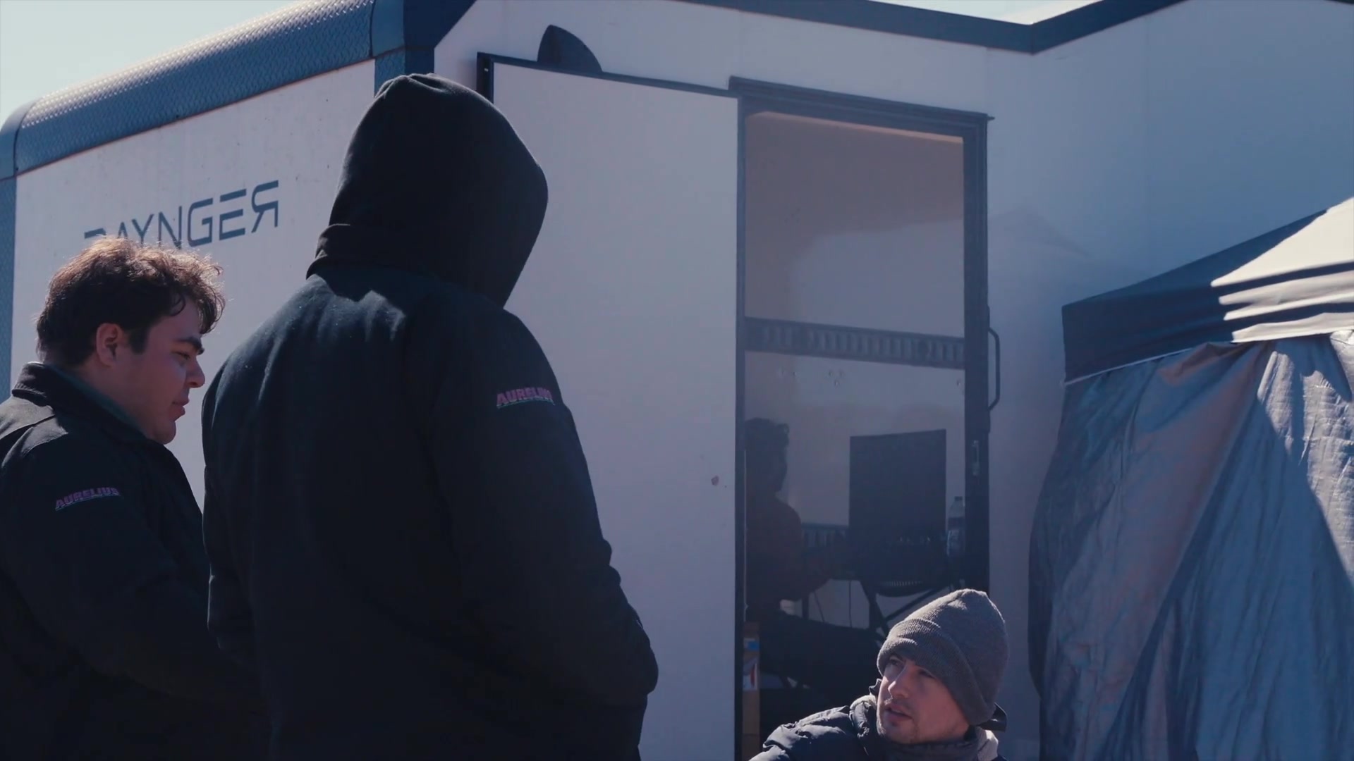 Aurelius-branded coworkers discussing field work beside a test trailer